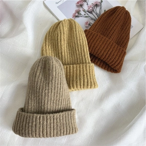 Knitted winter beanies in beige, yellow, and brown tones with vertical ribbing texture