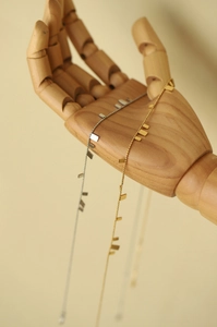 Artistic display of gold and silver square plate necklaces on a wooden hand model