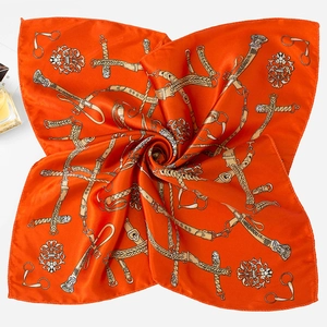 Detailed macro view of luxurious orange silk scarf with equestrian chain print pattern