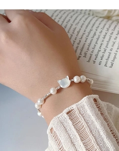 Close-up of s925 silver cat-shaped shell charm and freshwater pearl bracelet on a model