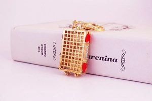 Close-up of golden suitcase keychain with red details on white book prop