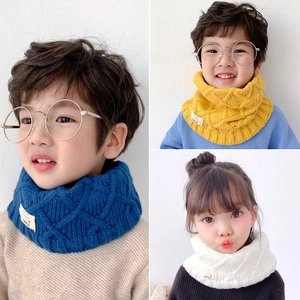 Detail of knit baby scarves in blue, yellow and white with diamond pattern and cute label
