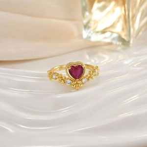 Close-up of golden ring featuring a heart-shaped ruby with micro-pave diamond accents