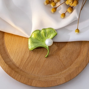 Detail of green ginkgo leaf brooch with pearl on a wooden tray and white fabric