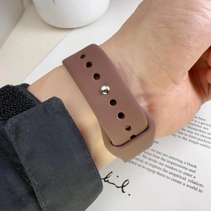 Detail of dark brown silicone sports watch band with silver pin-and-tuck closure on wrist