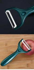Detail eines Edelstahl-Sparschälers mit grünem Griff auf einem roten Apfel und Holzbrett