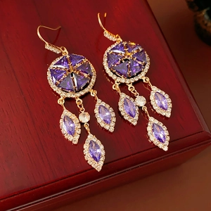 Close-up of vintage gold tassel earrings with purple zircons on a dark wood surface