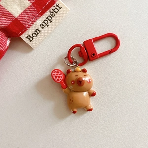 Close-up of cute resin capybara keychain with red tennis racket on textured surface