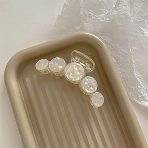 Detail of shell-textured acrylic hair claw clip with golden spring on beige tray