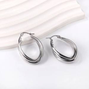 Polished stainless steel geometric twisted hoop earrings displayed on white stone platform
