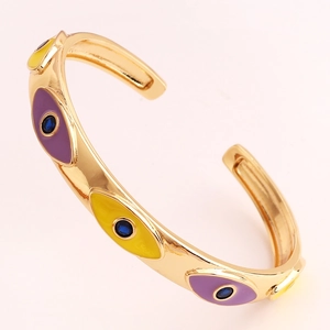 Close-up of golden enamel evil eye cuff bracelet with purple and yellow oil drip details