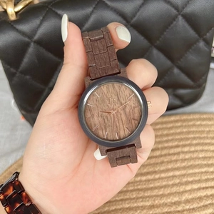 Handheld dark wood watch with gold hands and no numerals on a textured black background