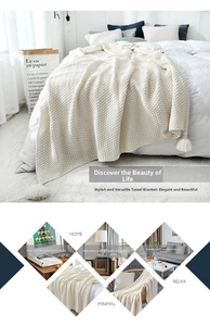 Detail of a beige chunky knit blanket featuring decorative large tassel ball fringe