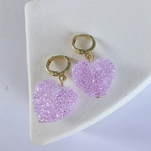 Close-up of sparkling purple crystal heart-shaped earrings with golden hoop closure