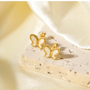 Macro view of gold butterfly earrings with white shell on elegant silk fabric