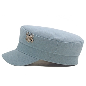 Détail de la casquette plate en jean bleu clair avec un badge d'araignée en métal argenté