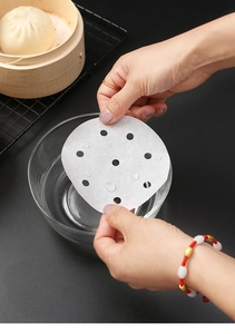 Close-up of waterproof round steamer paper liners with holes being held over a wooden steamer