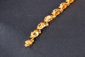 Macro shot of 3D skull links on a polished gold punk bracelet against a dark background