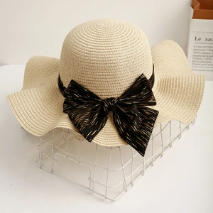 Detail of cream straw sun hat with large wavy brim and elegant black gold bow