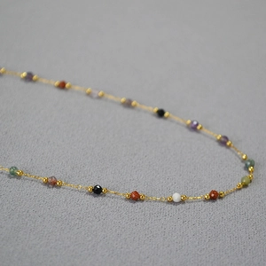 Macro detail of colorful natural stone beads on a dainty gold chain necklace