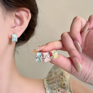 Close-up view of sweet bow-knot enamel hoop earrings in blue, pink, and yellow colors.