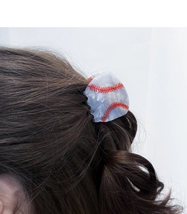Detail of white marble hair claw clip with red baseball stitching on brown wavy hair