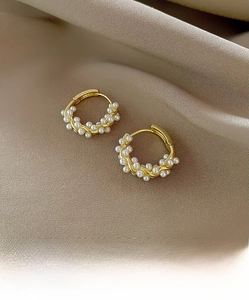 Macro view of gold hoop earrings with twisted design and micro white pearl inlay