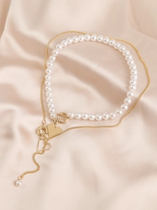 Detail of layered gold chain and pearl necklace with heart pendant on silk
