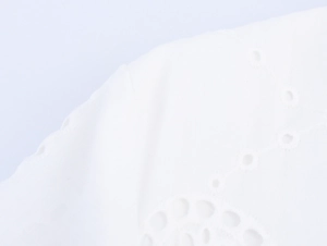 Close-up of white cotton fabric with detailed eyelet embroidery and wave patterns