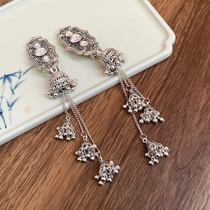 Close-up of ethnic silver tassel bell earrings on a vintage ceramic plate display