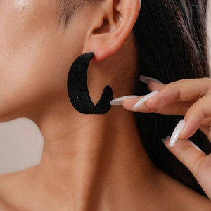 Close-up of black velvet C-shaped stud earrings on model showing matte texture