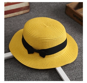 Dettaglio di un cappello di paglia intrecciato con nastro nero su uno sfondo grigio