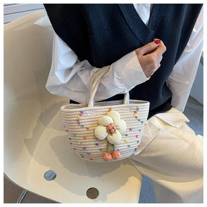 Detail of hand-woven beige cotton tote with colorful pom-poms and floral charm