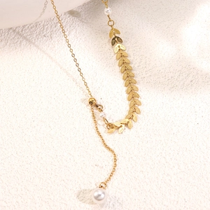 Macro detail of gold leaf chain with three white pearls on a white stone background