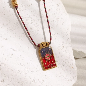 Detail of bohemian tarot sun necklace on white stone with red blue braided rope chain