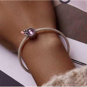 Macro view of woven silver bracelet featuring faceted purple crystal and heart charm