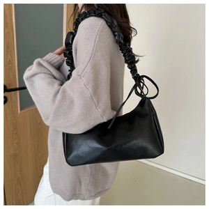 Close-up of black shoulder bag featuring unique pleated strap detail worn by a model