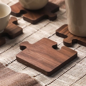 Puzzle-Untersetzer aus schwarzem Walnussholz auf kariertem Tuch mit Keramiktasse