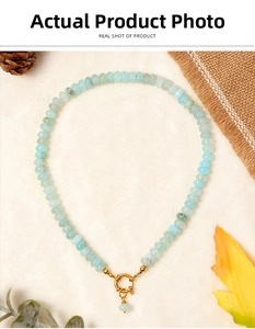 Close-up of aquamarine beaded necklace with a golden round buckle on a rustic fabric background