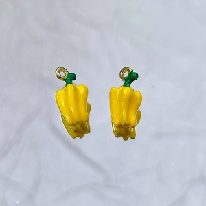 Macro detail of two vibrant yellow chili pepper pendants with green stems and gold loops