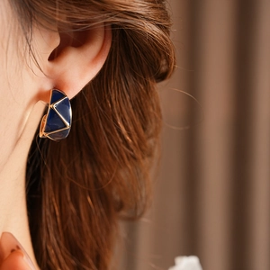 Detail of C-shaped gold metal earrings with deep blue enamel and geometric patterns