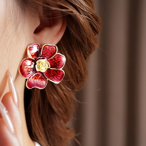 Primer plano de pendientes de flores vintage en esmalte rojo con borde dorado en una modelo
