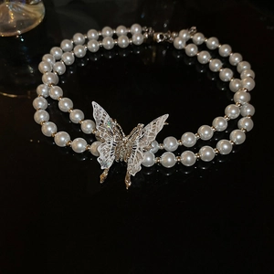 Macro detail of a double-layer pearl necklace with a shimmering butterfly pendant