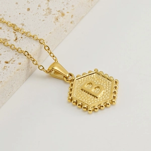 Detail of a gold hexagonal letter B pendant necklace with a beaded edge on a fine chain