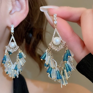 Macro detail of gold tassel earrings with blue beads and pearls worn by a model