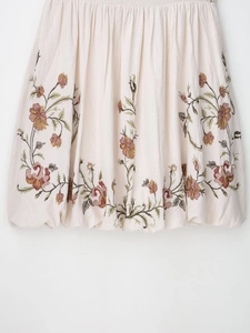 Close-up of floral embroidery on the hem of an ivory short dress with fabric details
