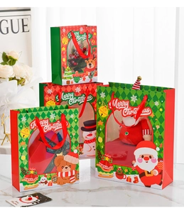 Detailed view of Christmas gift bags with PVC window and red ribbon handles on marble surface