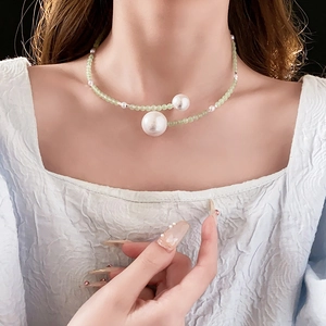 Close-up of minimalist pearl necklace with light green beads on white textured clothing