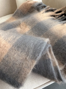 Close-up texture of soft beige and grey plaid scarf with decorative fringe details