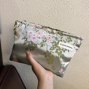 Floral satin cosmetic bag with silk texture and green floral pattern held by hand